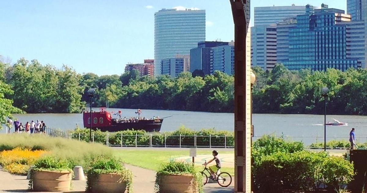 una persona que va en bicicleta junto a un río con un bote