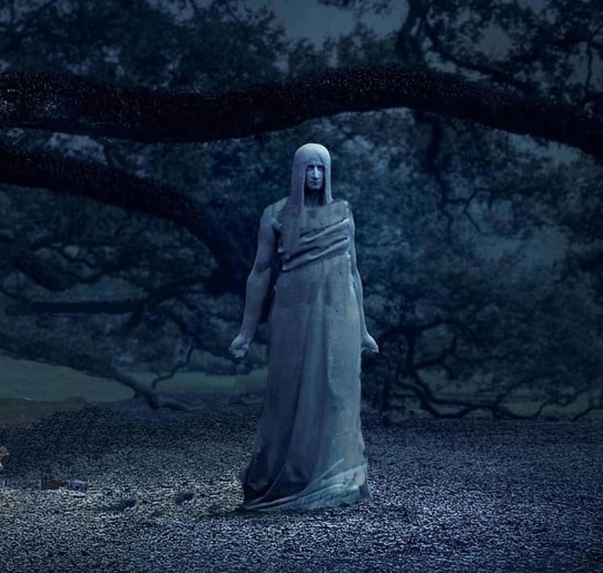 uma estátua de uma mulher em pé em frente a uma árvore