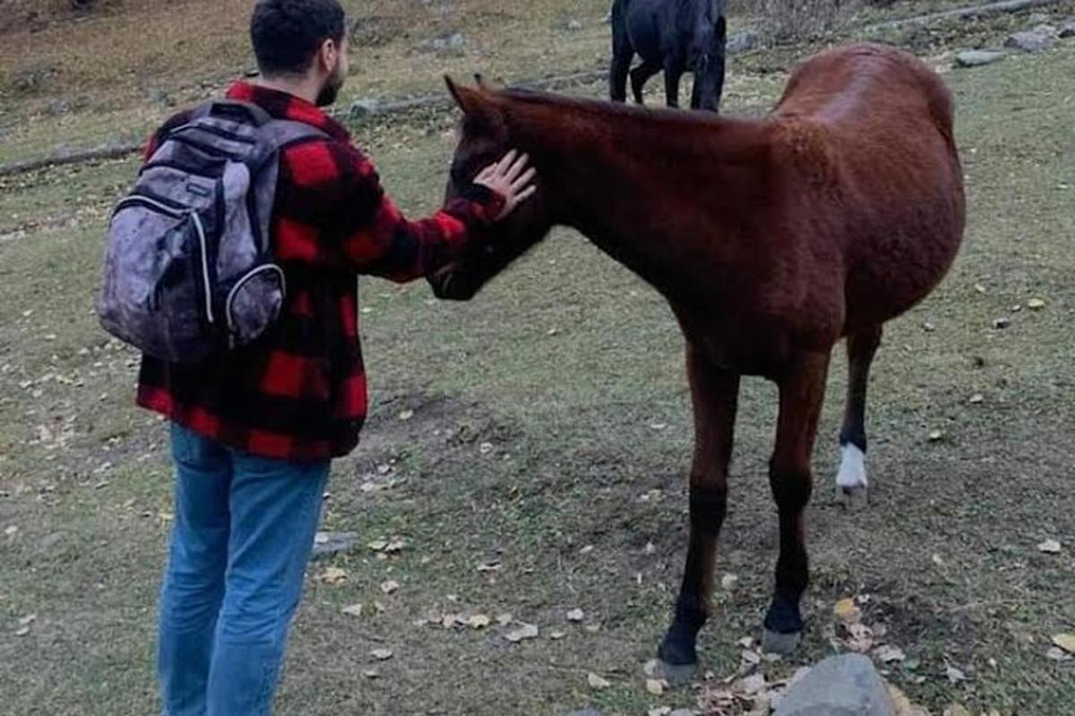 um homem com uma mochila acariciando um cavalo marrom