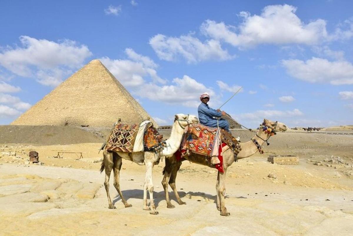 muž jedoucí na velbloudovi před pyramidami