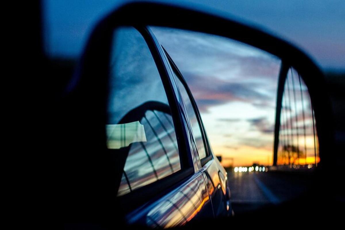 uno specchietto retrovisore laterale di un'auto con il riflesso del tramonto