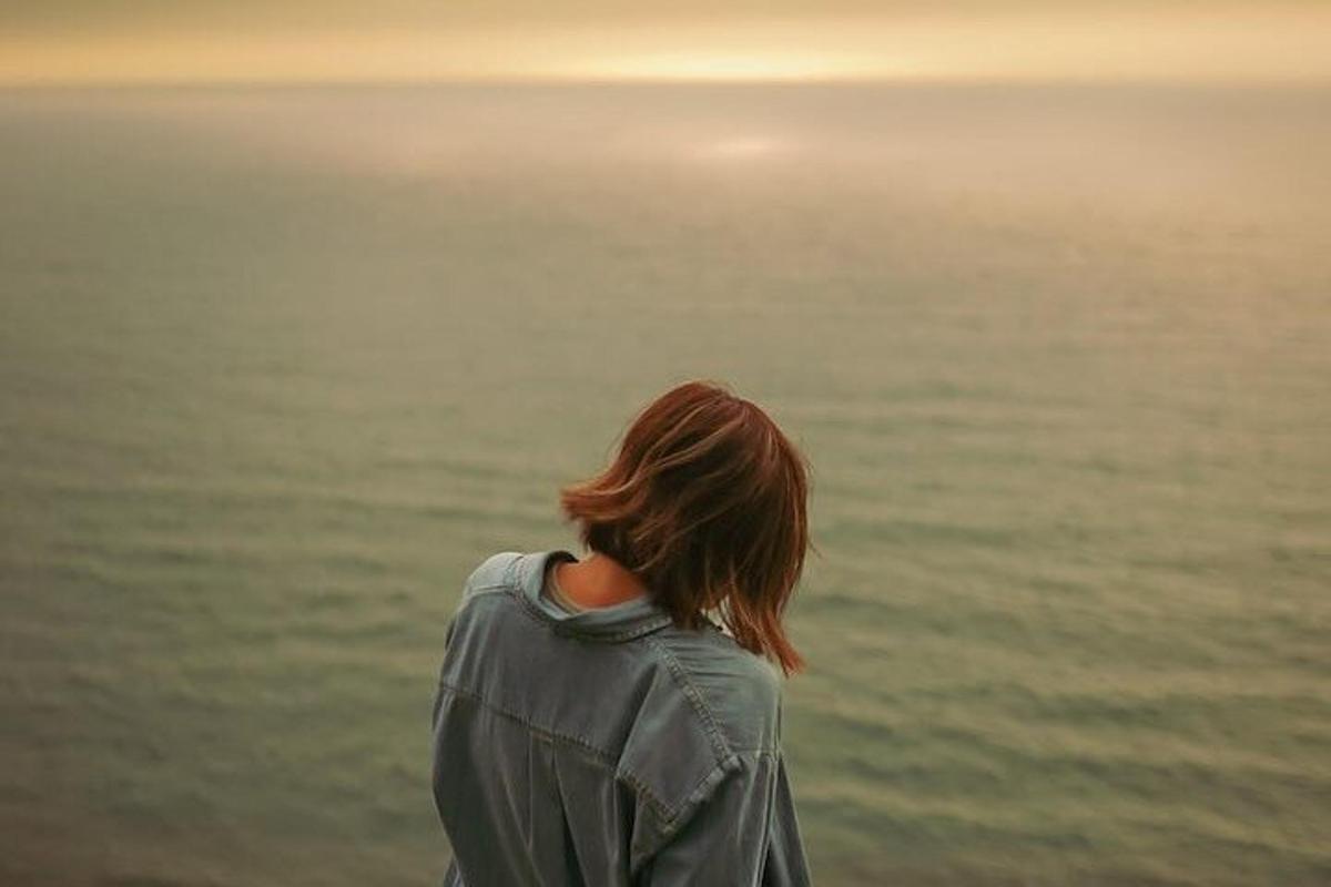 Una mujer mirando el océano al atardecer.