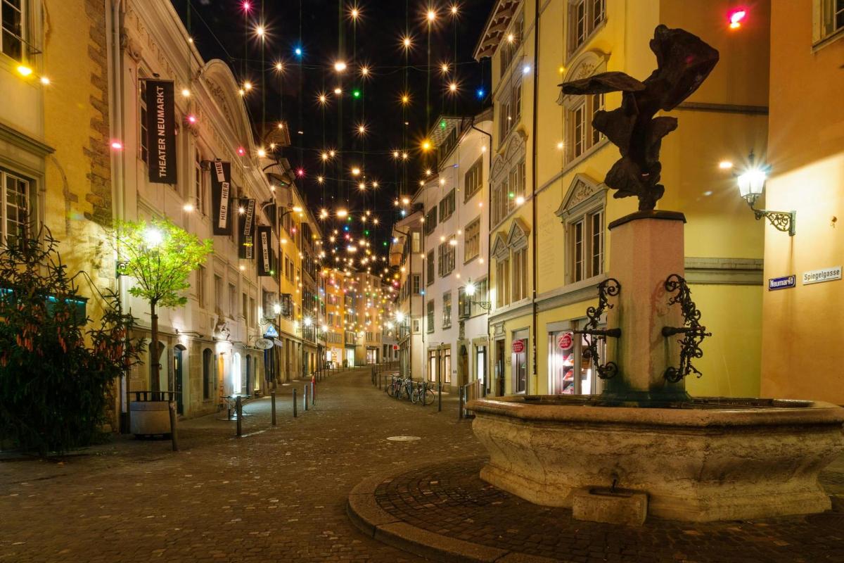 Una calle con una fuente en medio de una ciudad por la noche.