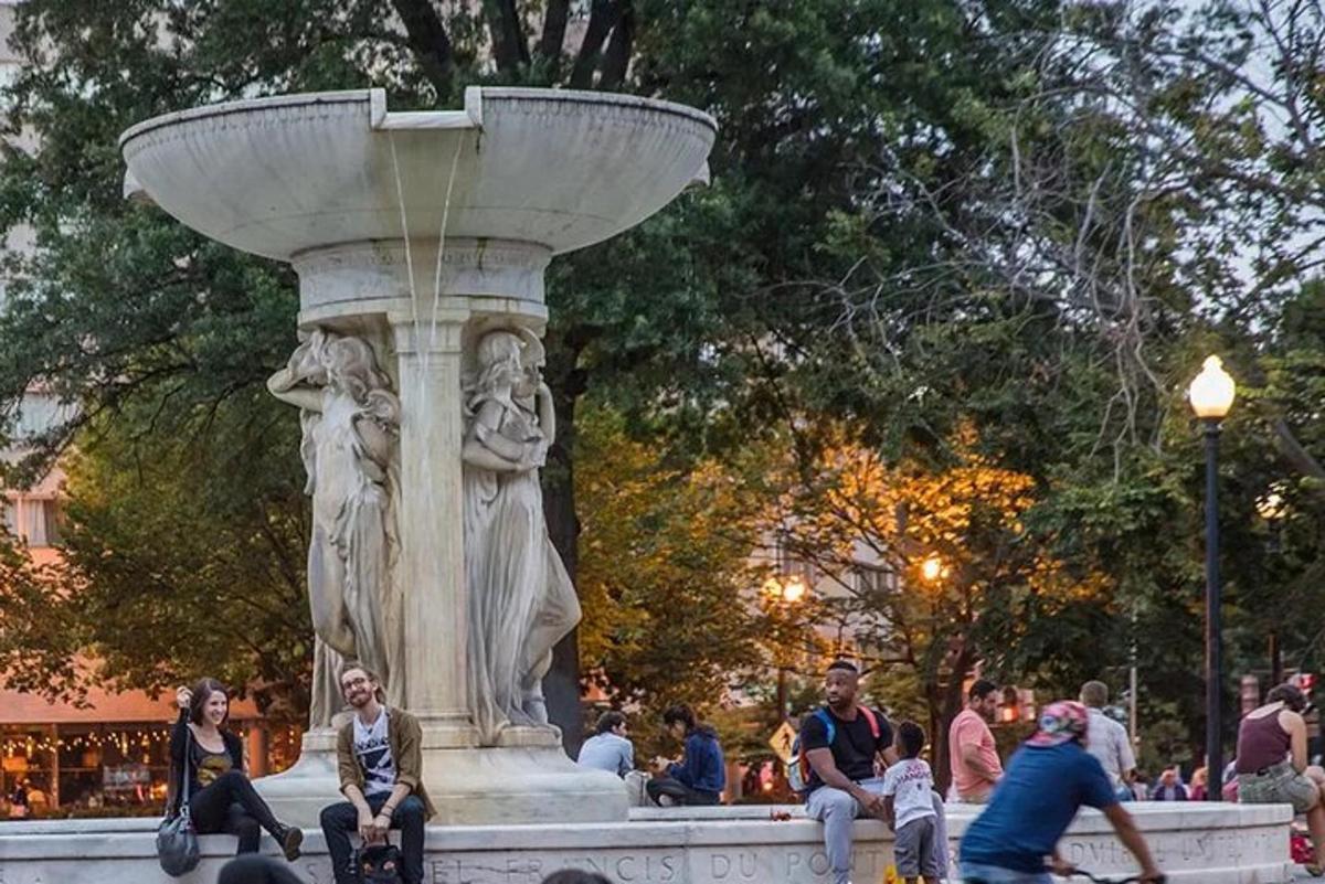 μια ομάδα ανθρώπων που κάθονται γύρω από ένα σιντριβάνι σε ένα πάρκο