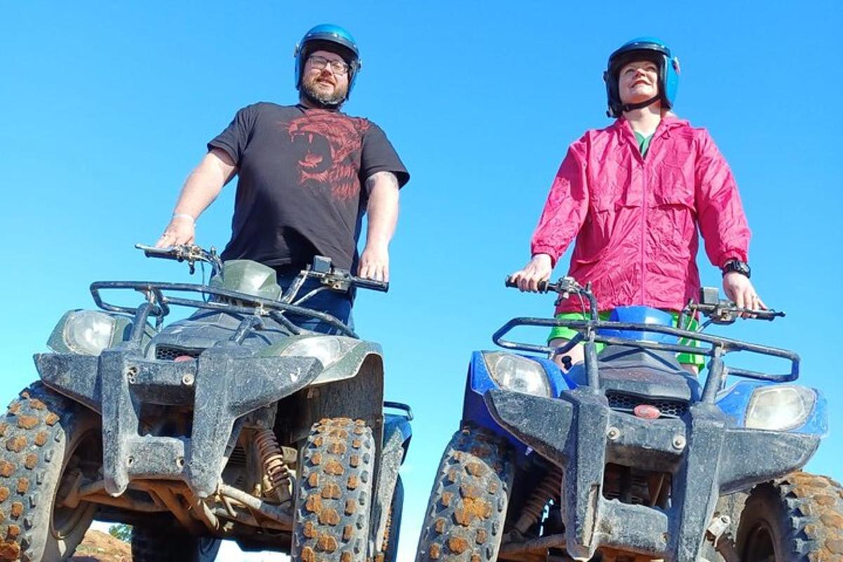 two men standing next to two atvs
