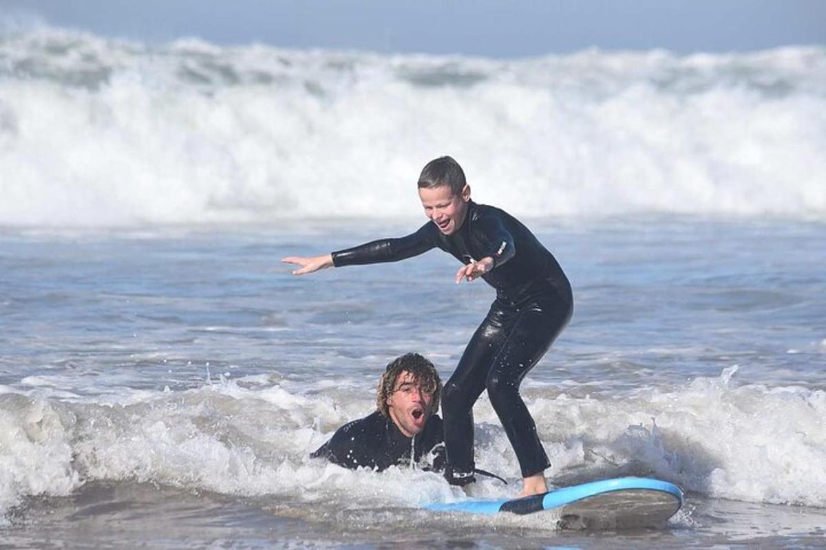 a boy on a surfboard next to a man in the ocean