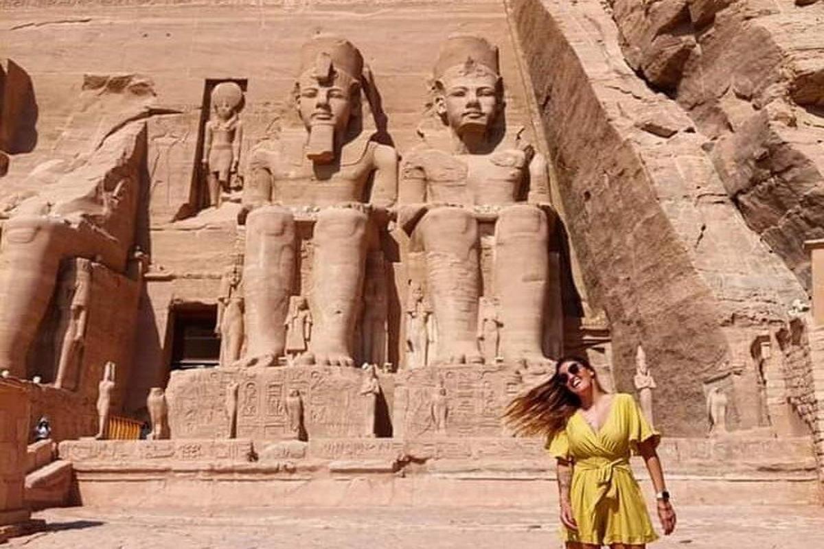 uma mulher de vestido amarelo em pé em frente a uma estátua