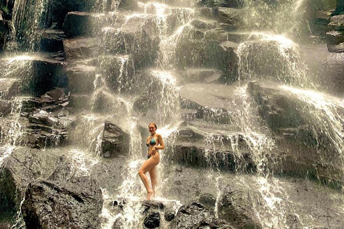 ženska v bikiniju stoji pred slapom