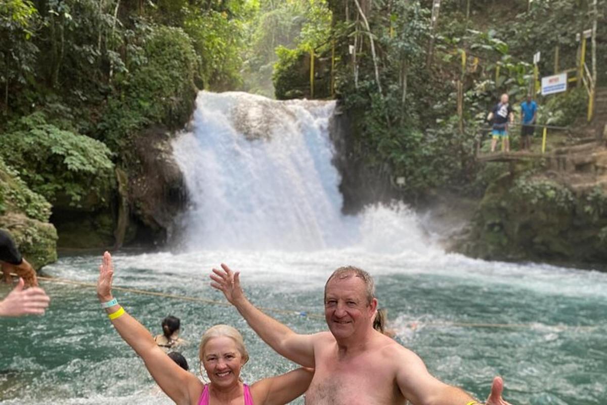 um homem e uma mulher na água em frente a uma cachoeira