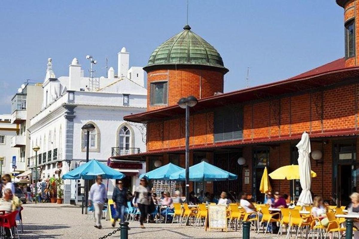 skupina lidí procházejících kolem budovy se stoly a slunečníky