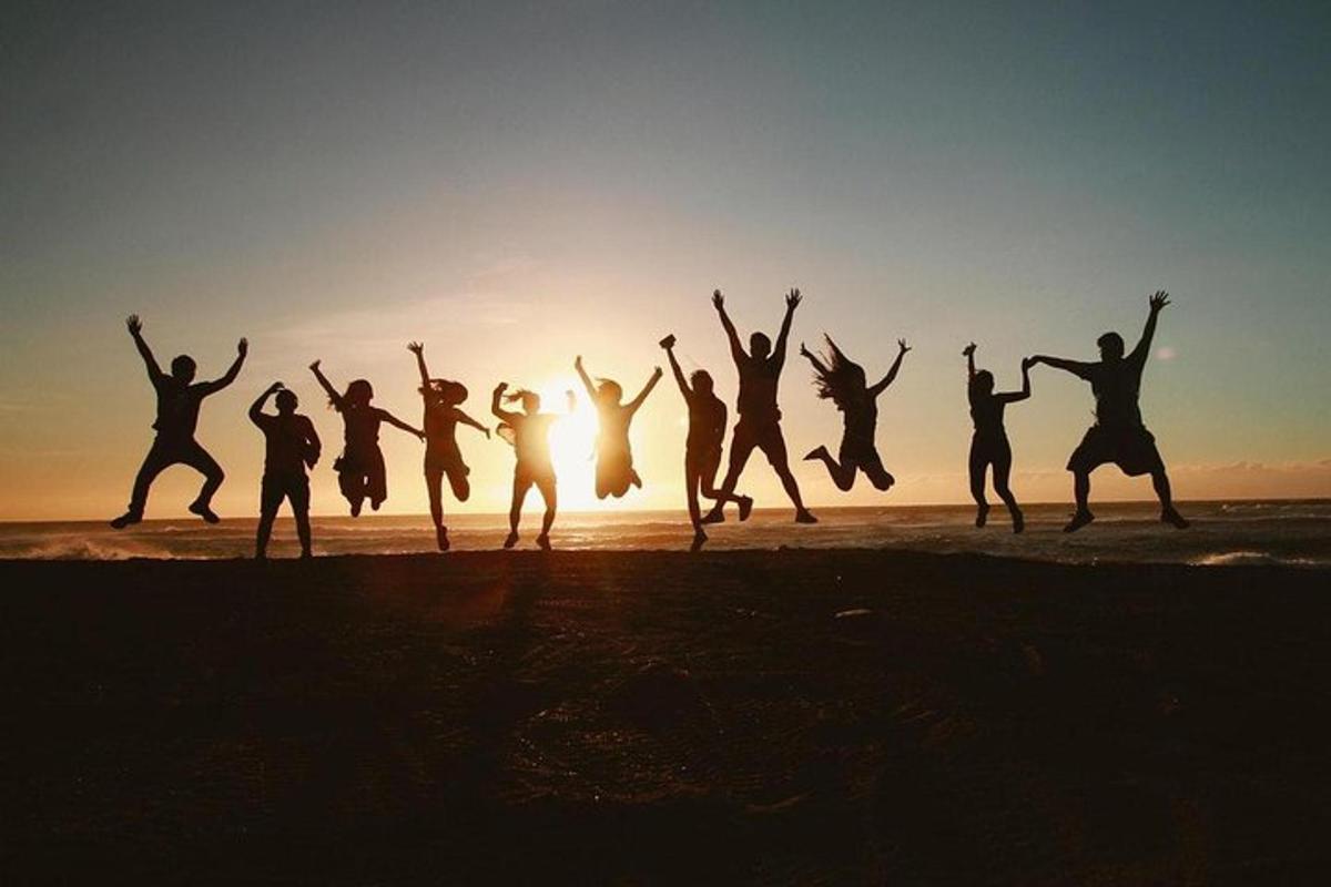 a group of people jumping on the beach at sunset