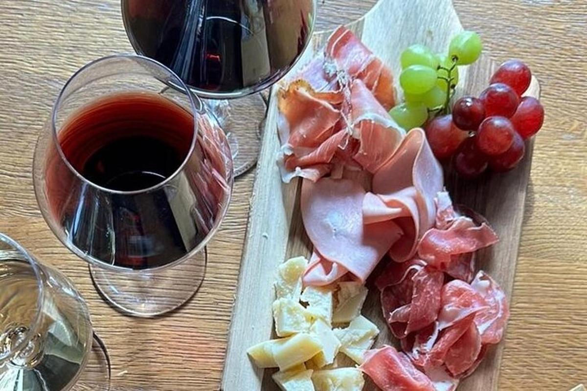 en skärbräda med kött och vindruvor och ett glas vin