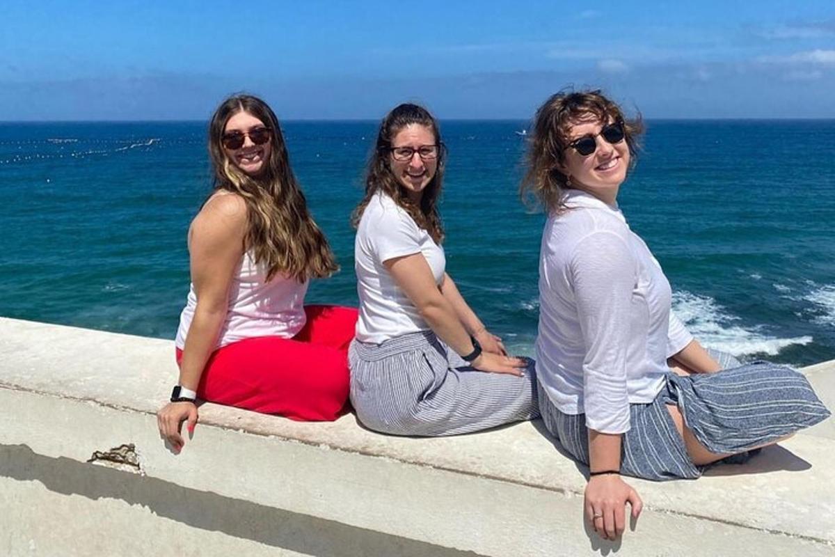 tiga wanita duduk di dinding di tepi laut