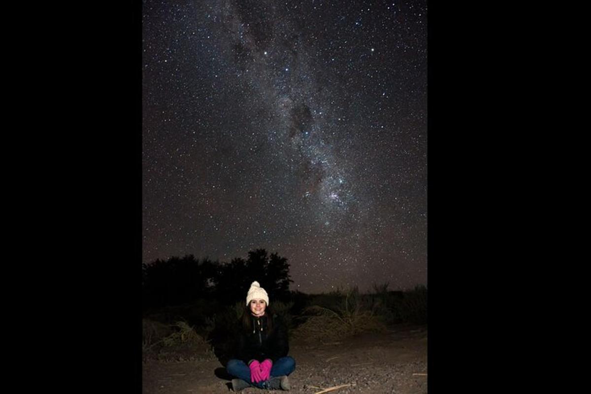 a woman sitting on the ground looking up at the night sky