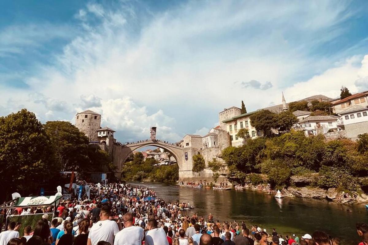 ένα πλήθος ανθρώπων που στέκονται σε ένα ποτάμι με μια γέφυρα