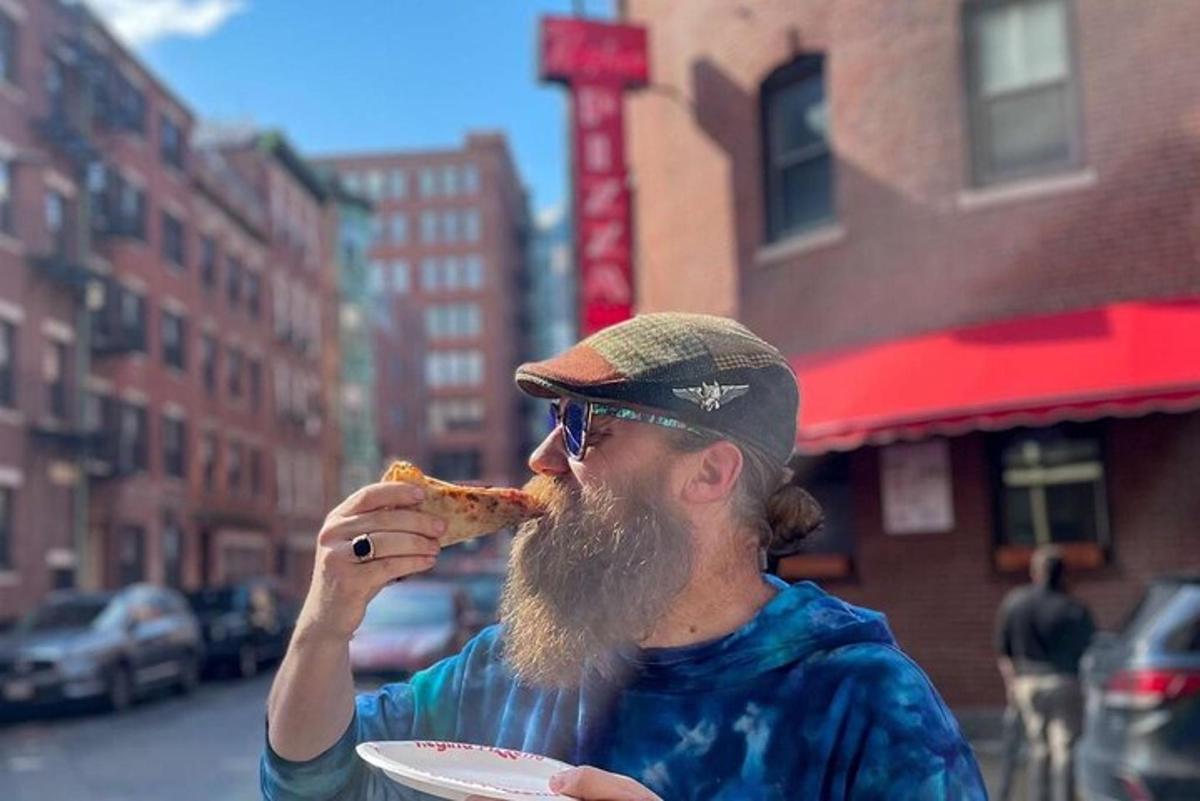 muž s vousy jí kousek pizzy