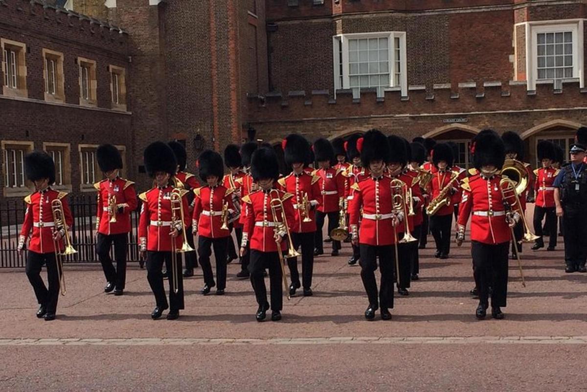 maršējošais orķestris sarkanās uniformās iet ēkas priekšā