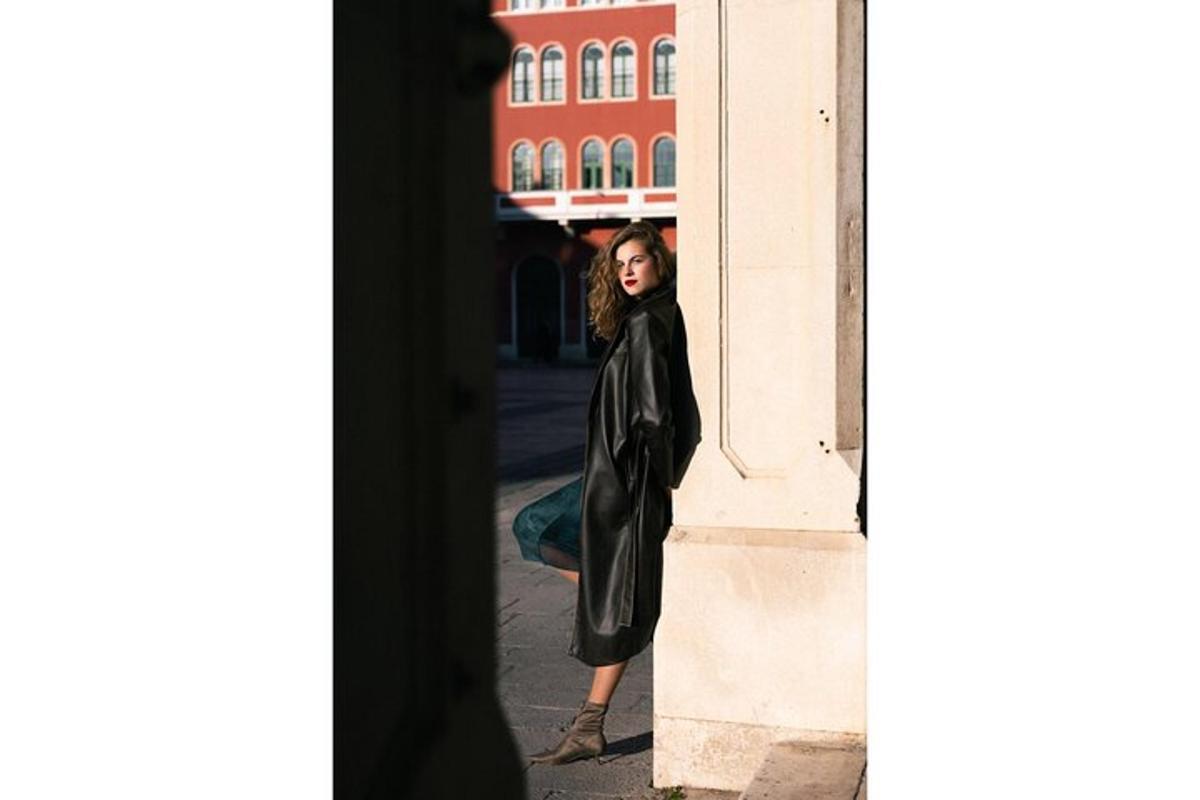 a woman in a black coat leaning against a wall