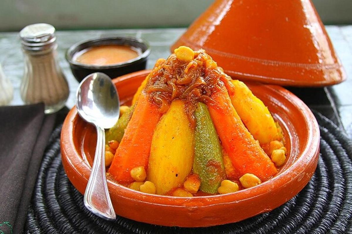 an orange bowl of fruit and vegetables with a spoon