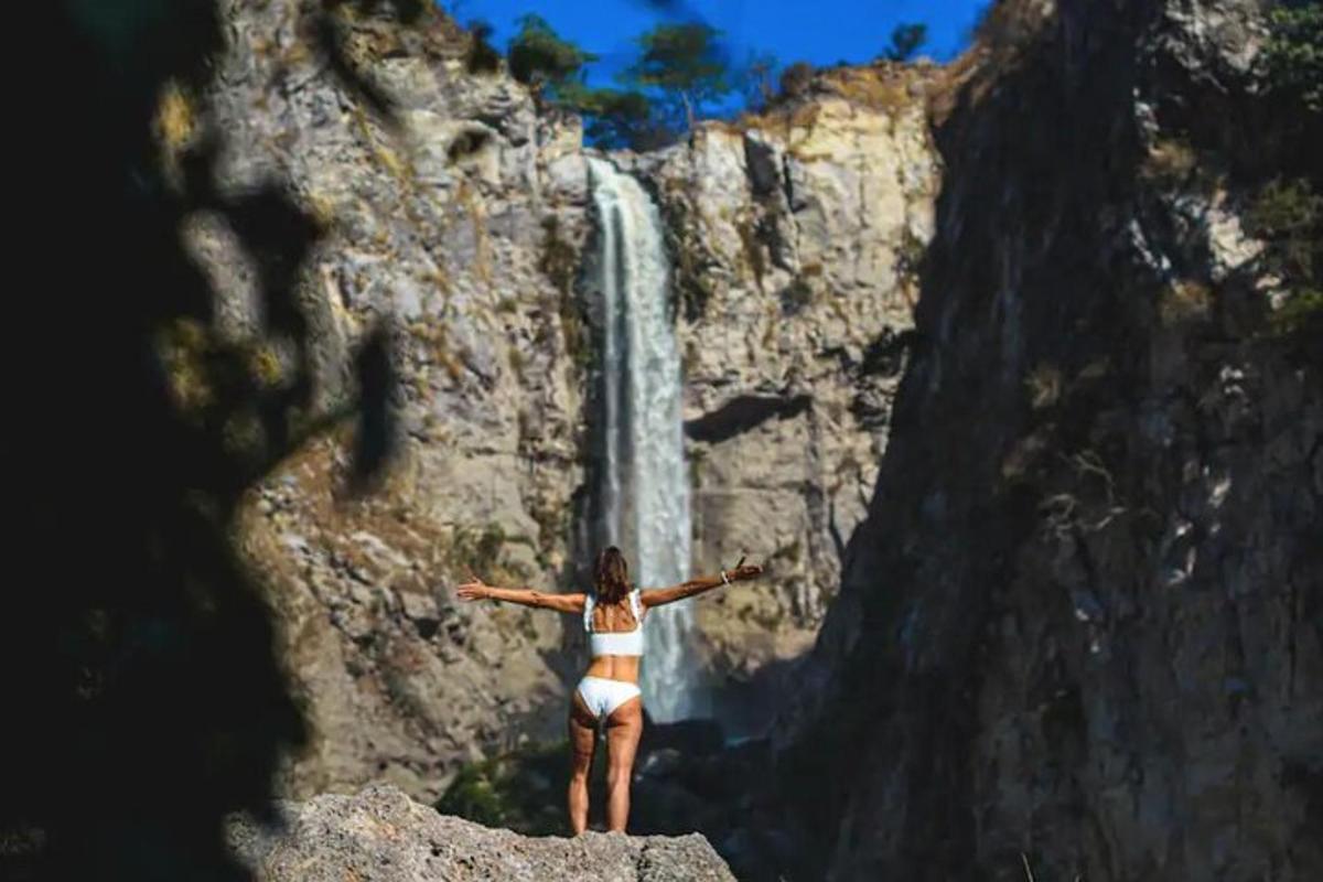 uma mulher em pé sobre uma rocha em frente a uma cachoeira