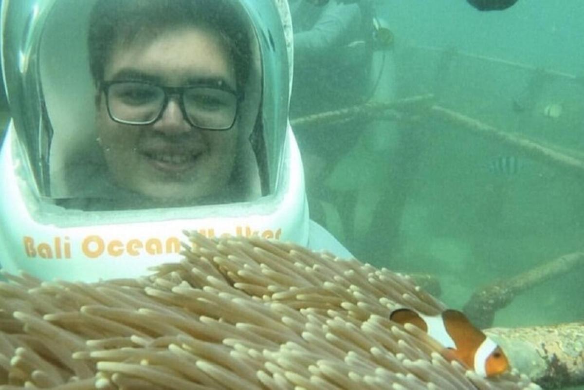 a man in glasses looking at a goldfish in a fish tank