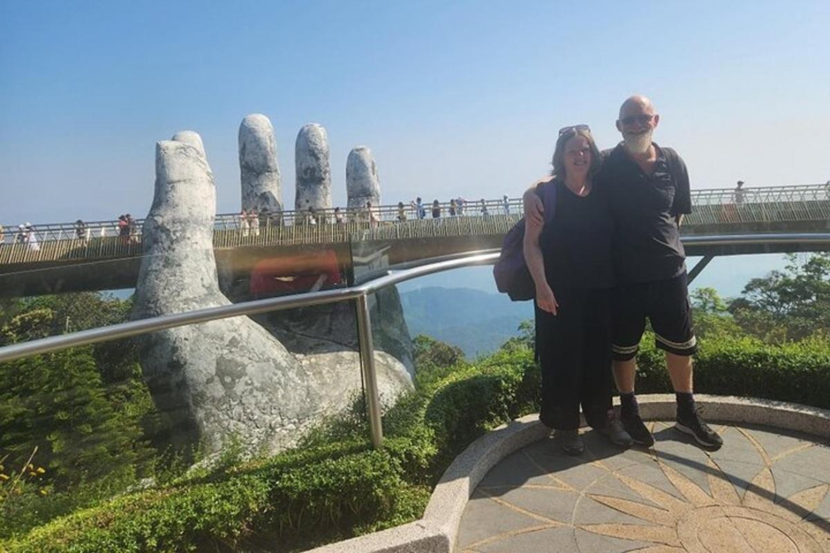 Un hombre y una mujer de pie frente a un puente con una estatua de manos.