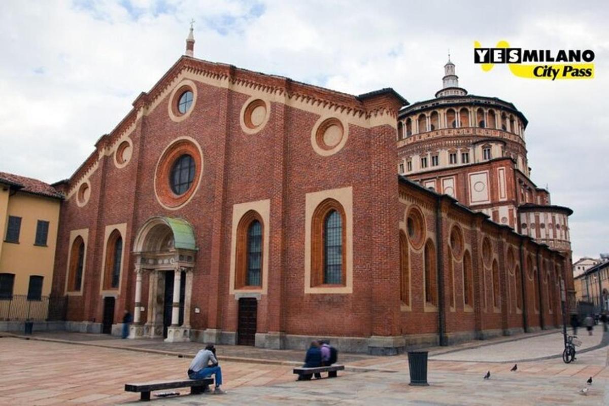 tři lidé sedící na lavičkách před cihlovou budovou