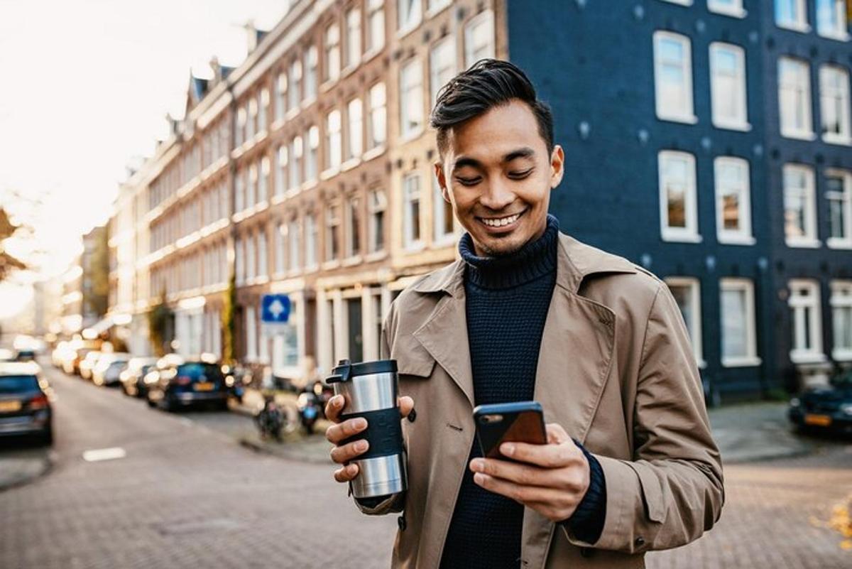 mees hoiab käes tassi ja vaatab oma mobiiltelefoni
