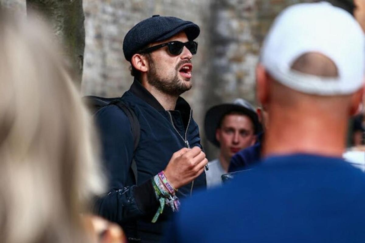 a man wearing a hat and sunglasses speaking to a group of people
