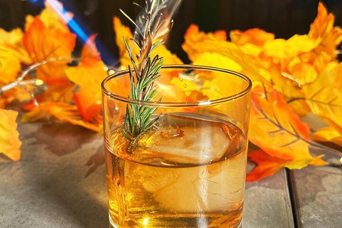 a glass of whiskey with rosemary in it on a table