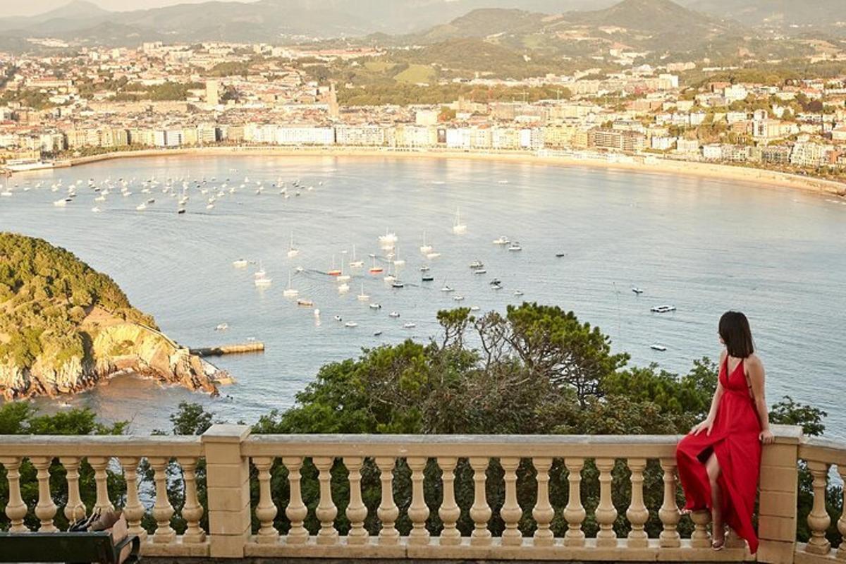 una dona amb un vestit vermell asseguda en una tanca mirant una platja
