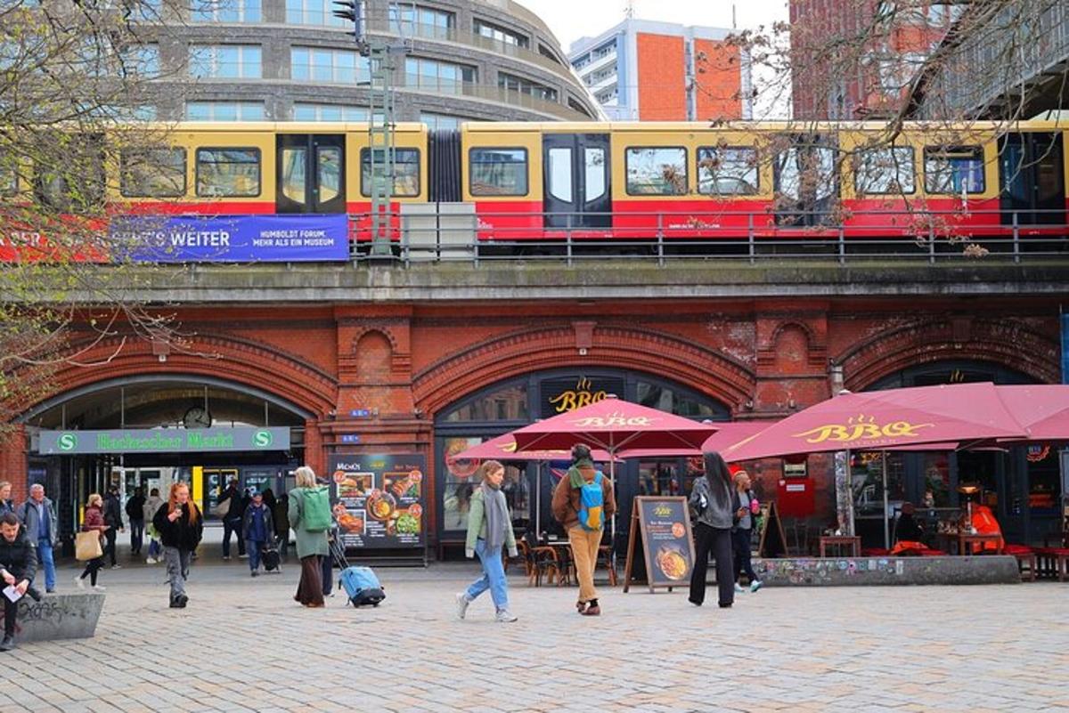 people walking on a street with a train on a bridge