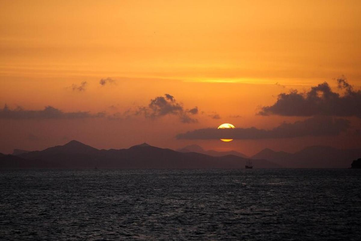 a sunset over the ocean with mountains in the background