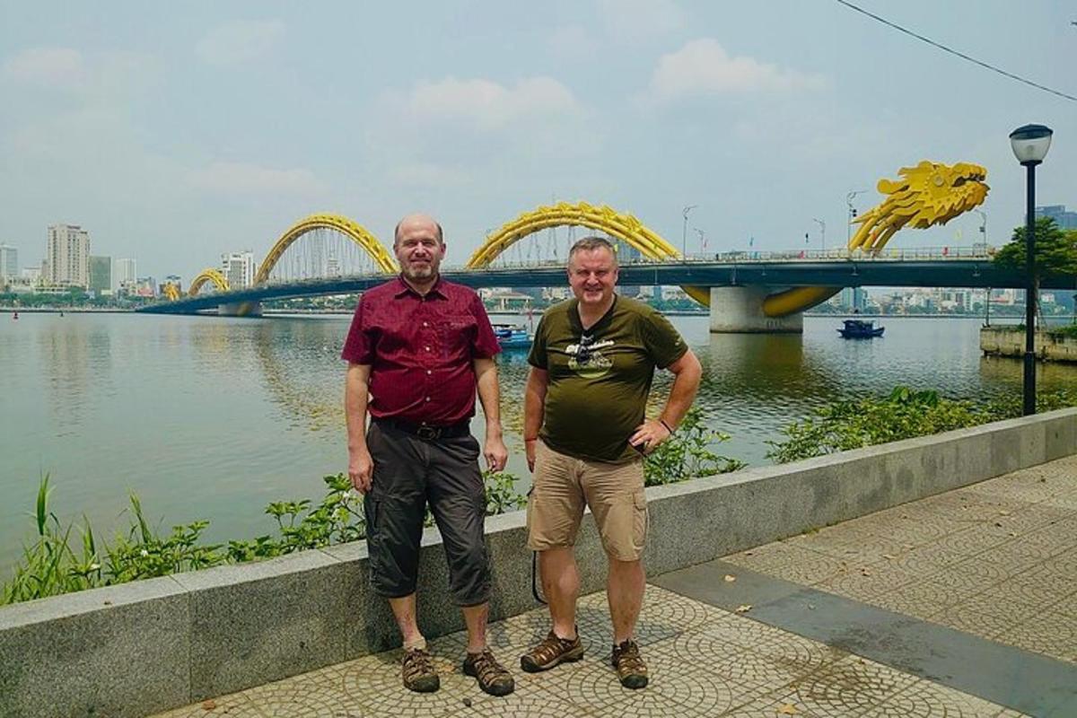 dois homens parados perto de um rio com uma ponte