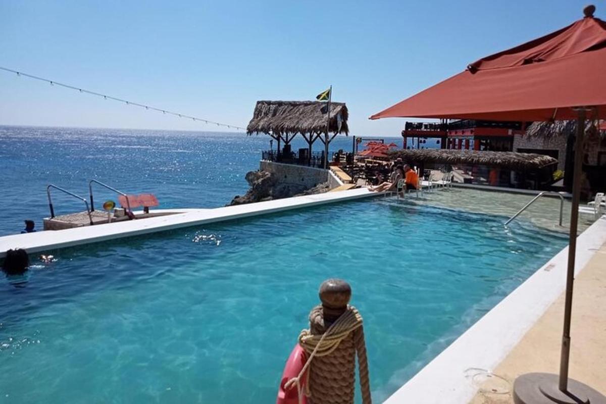 seorang wanita berdiri di samping kolam renang di samping laut