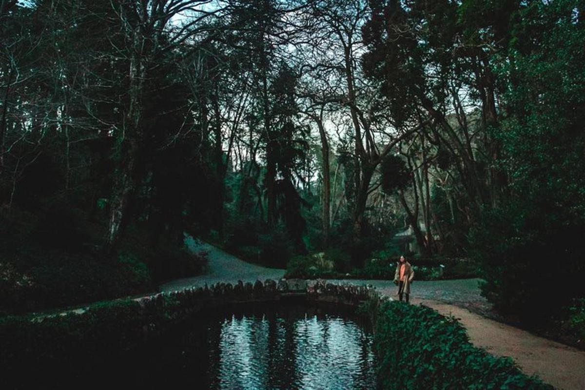 Un hombre parado junto a un estanque en un bosque.