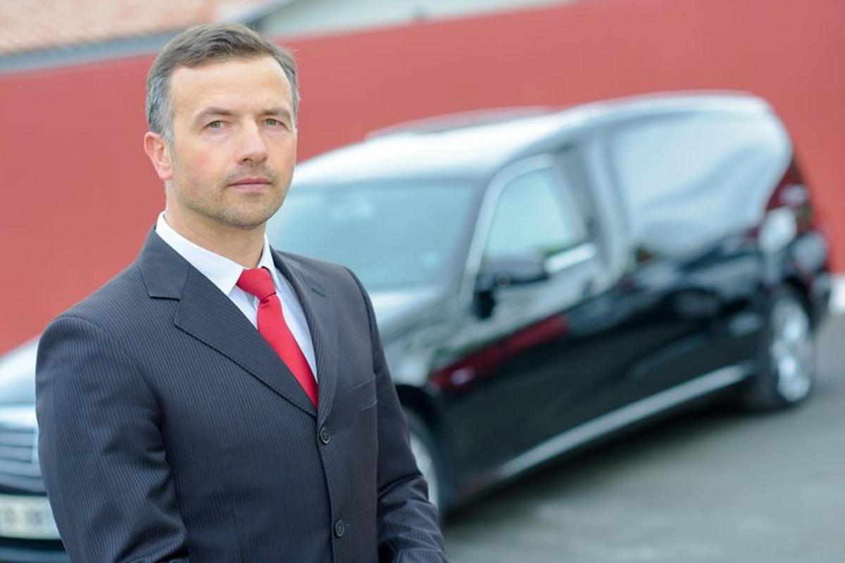muž v obleku a kravatě stojící před autem