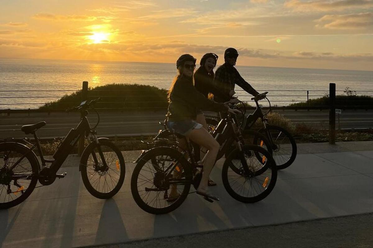 três pessoas andando de bicicleta em uma calçada perto do oceano
