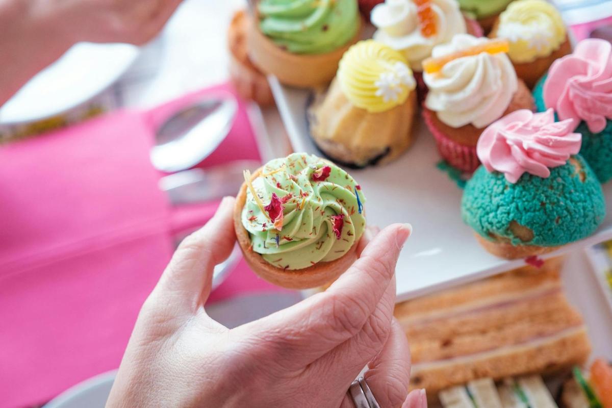 una persona che tiene in mano un cupcake davanti a un piatto di cupcake