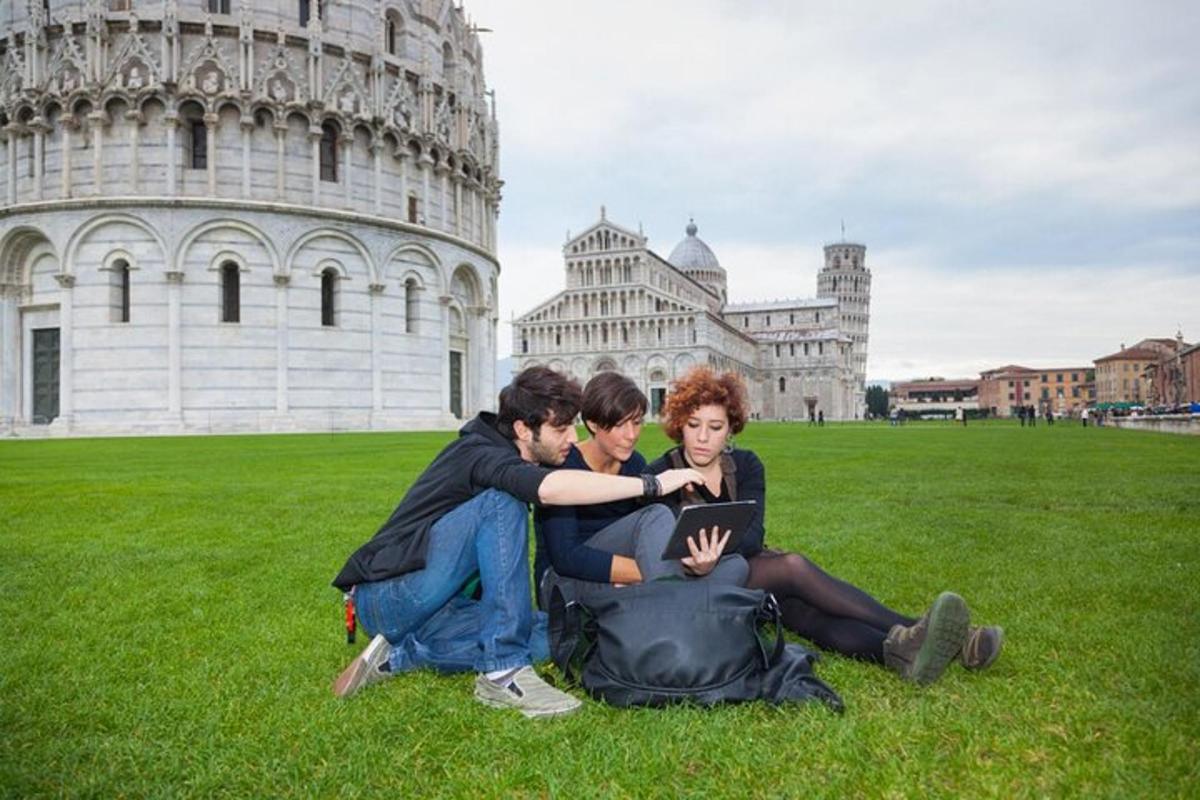 three people sitting on the grass in front of the leaning tower