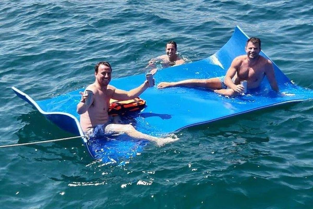 tři muži ležící na modrém surfovém prkně ve vodě