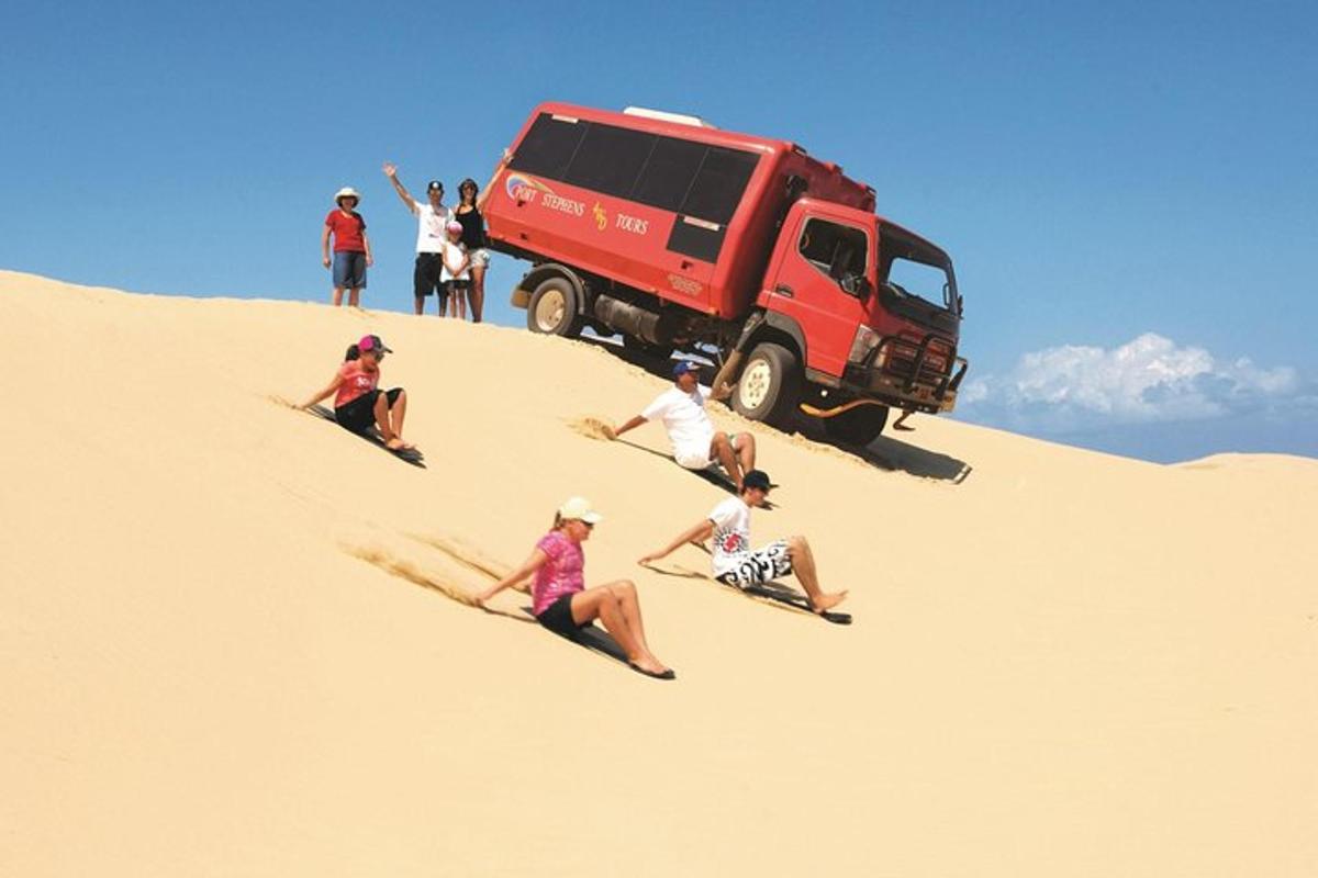 a group of people sitting in the sand in front of a red truck
