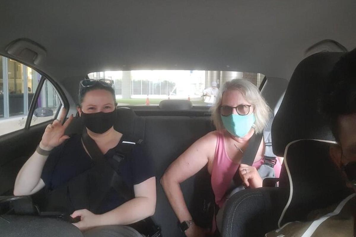 two women sitting in a car wearing masks