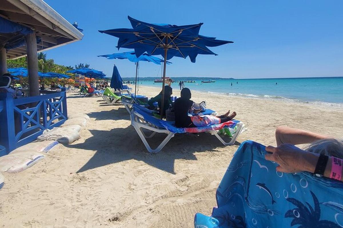 skupina ljudi, ki sedijo na stolih pod senčnikom na plaži