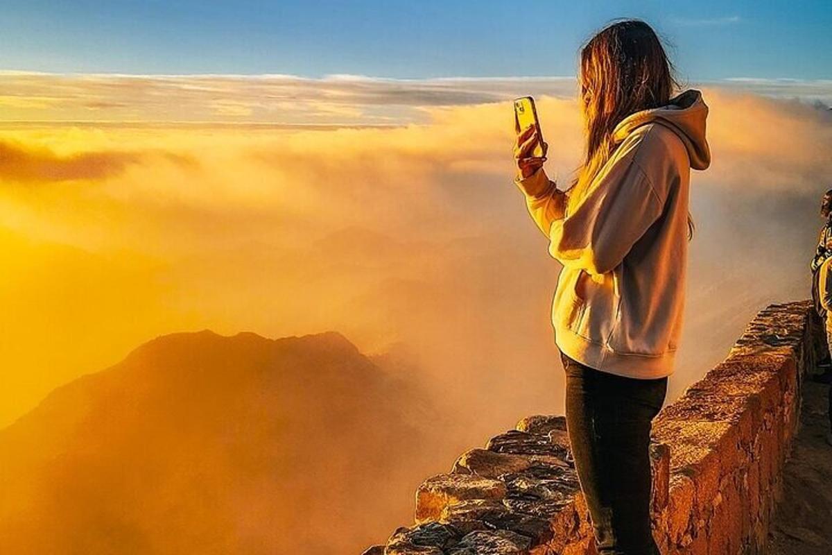 sieviete, kas stāv kalna virsotnē un fotografē