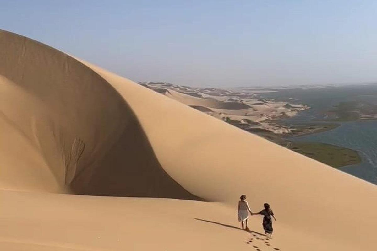 two people walking on top of a sand dune