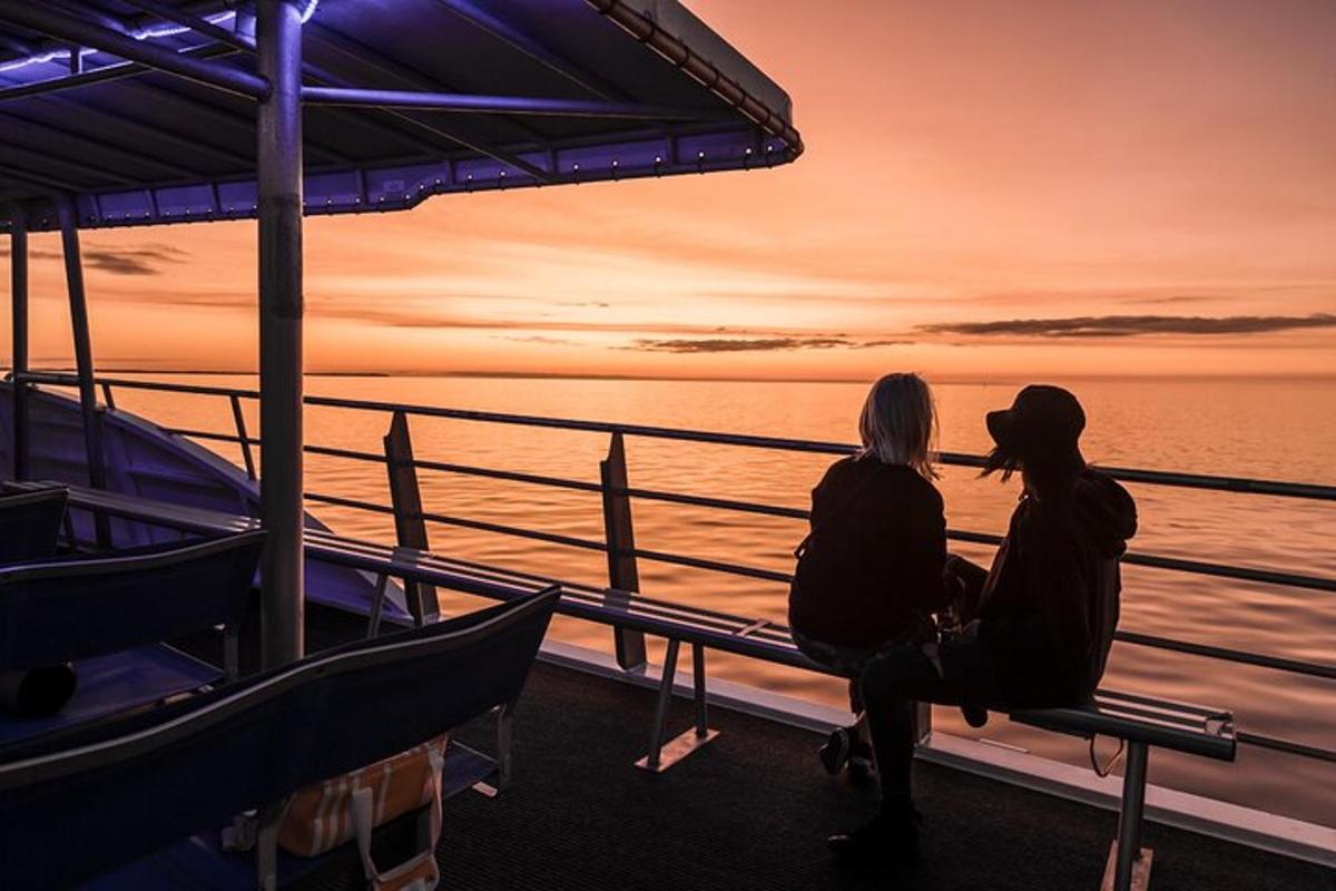 two people sitting on a bench on a ship looking at the ocean