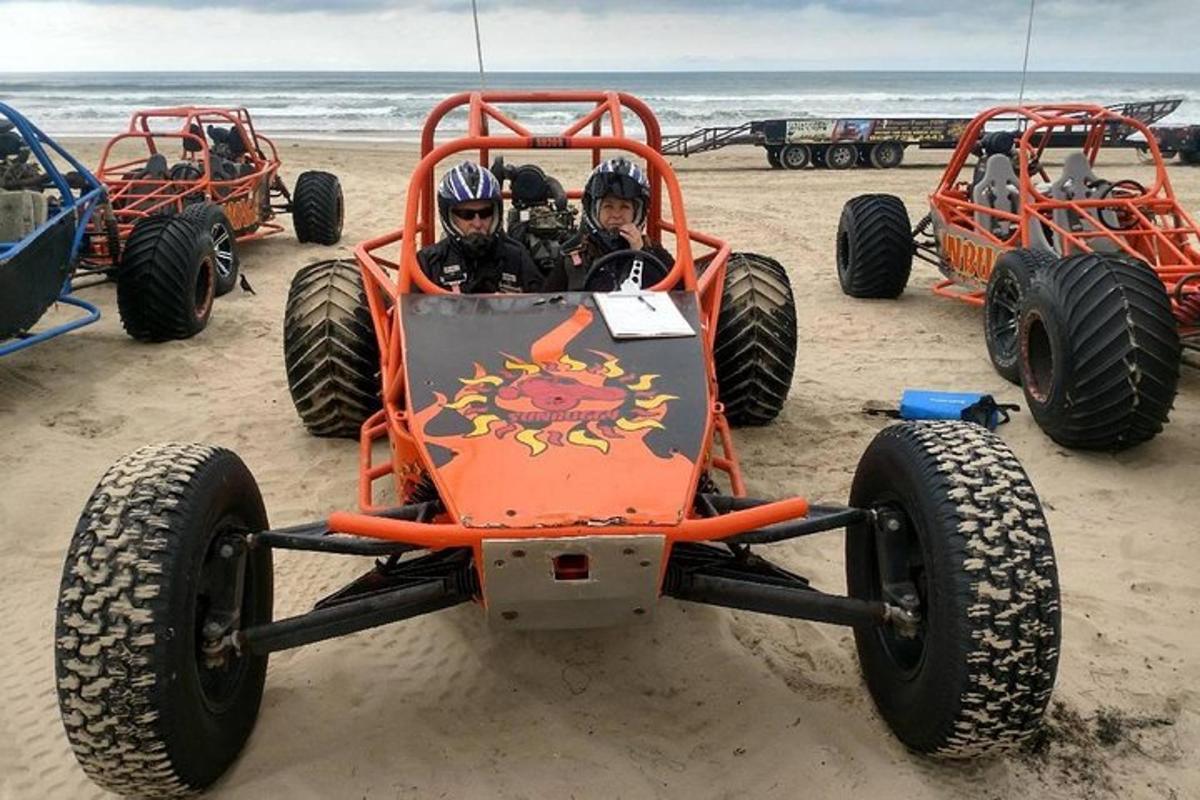 two people riding in an orange car on the beach