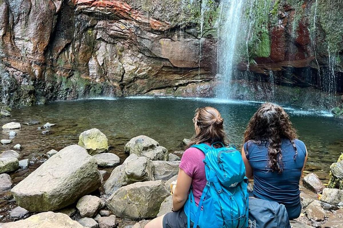 duas mulheres sentadas em pedras perto de uma cachoeira