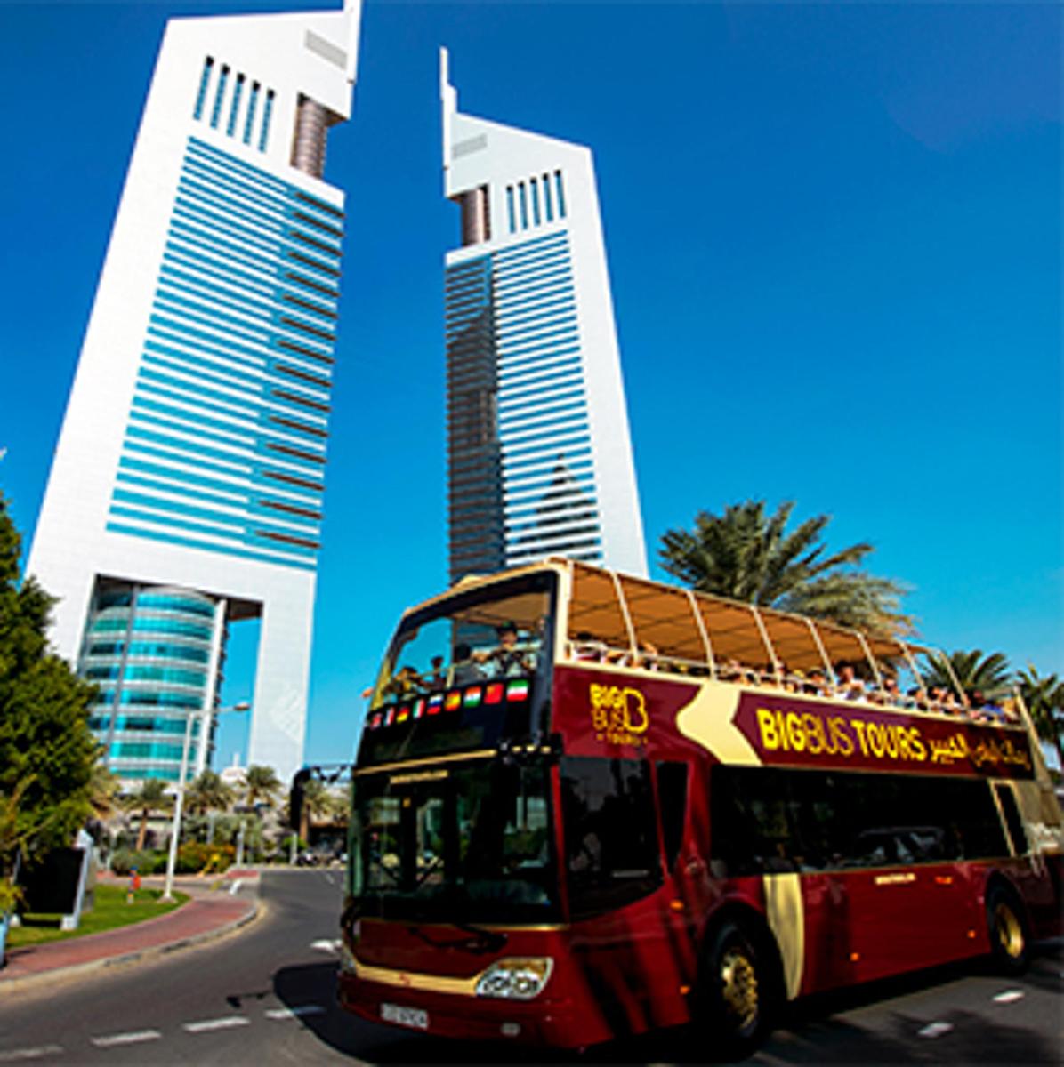 a red double decker bus driving down a street with tall buildings